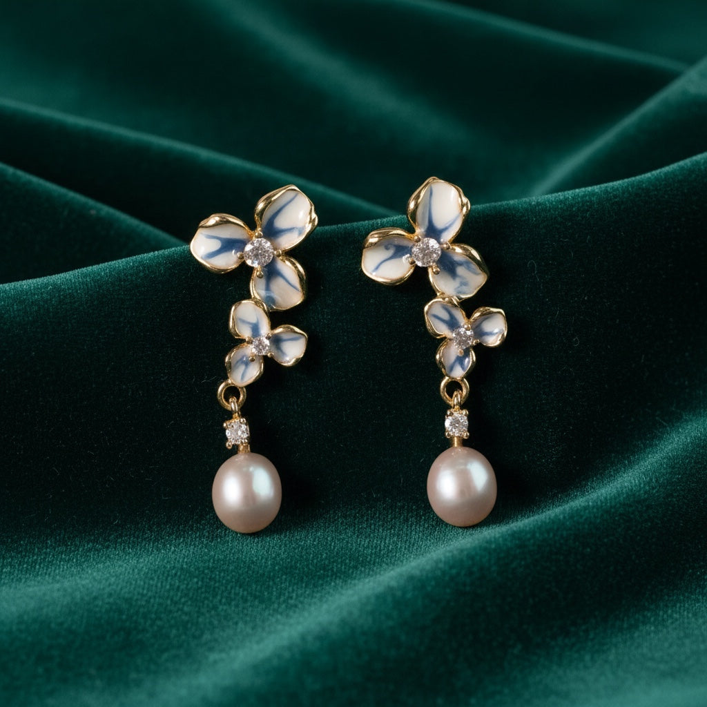 Charmluna floral drop earrings with white and blue enamel petals, cubic zirconia, and pearls on green velvet.