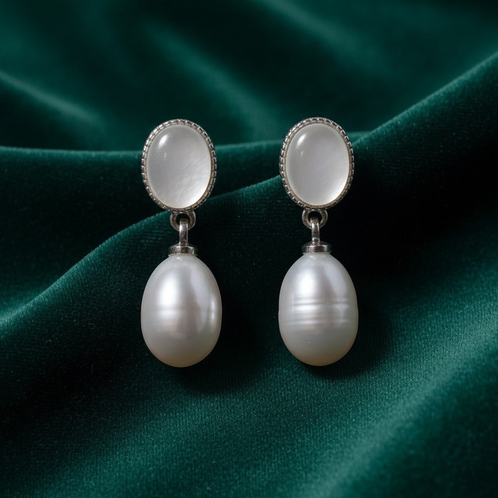 Charmluna silver oval mother of pearl stud earrings with luminous pearl drops on a dark green velvet background.