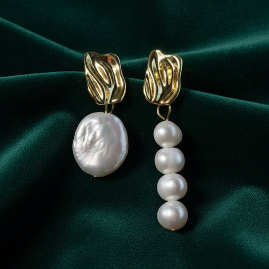 Charmluna asymmetric baroque pearl statement earrings with sculptural gold tops on a dark green velvet background.