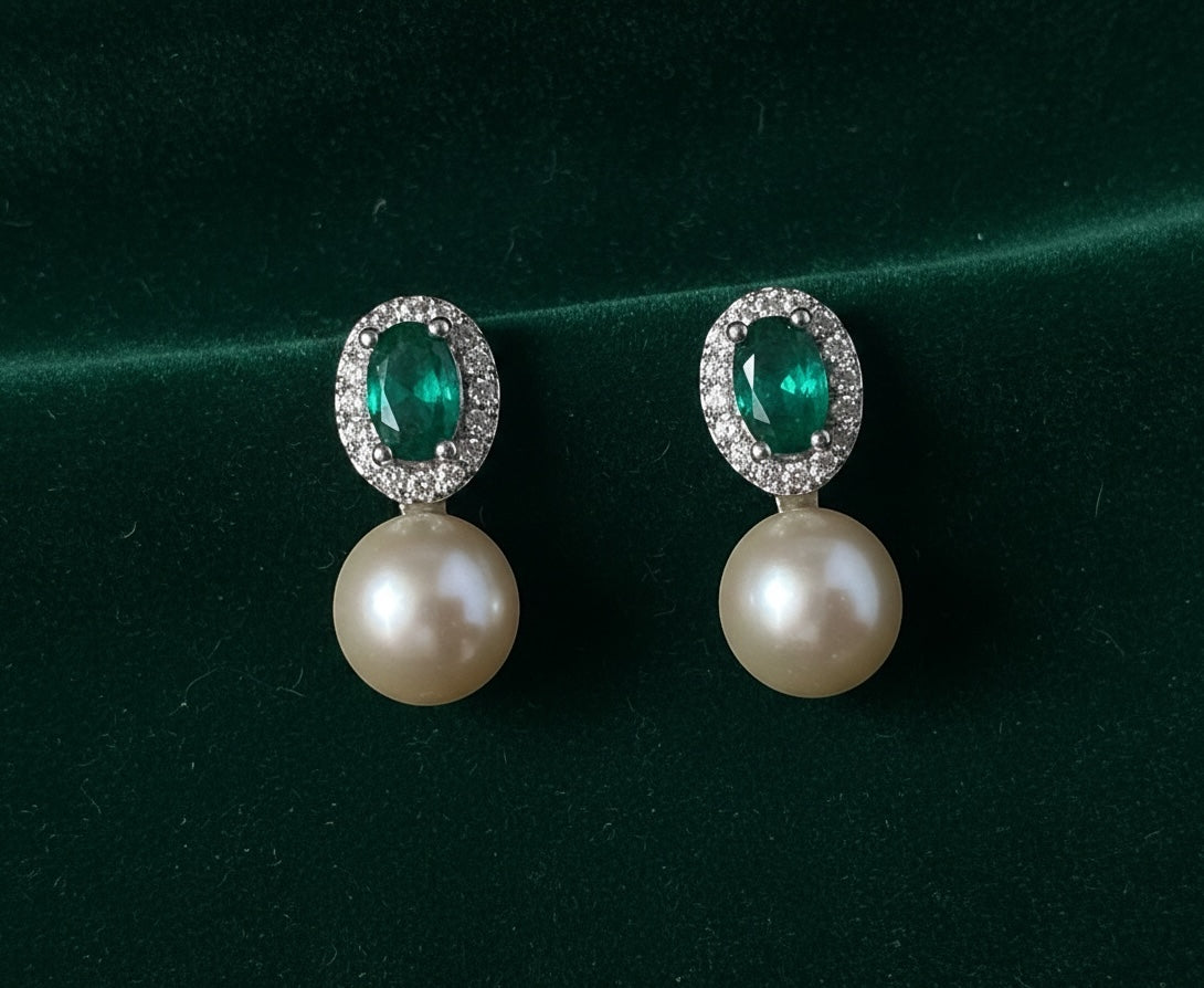 Charmluna emerald oval crystal drop earrings with a sparkling halo and lustrous white pearl on green velvet.