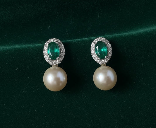 Charmluna emerald oval crystal drop earrings with a sparkling halo and lustrous white pearl on green velvet.