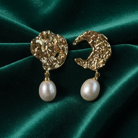 Charmluna sculptural gold-tone hammered crescent earrings with organic white baroque pearl drops on green velvet.