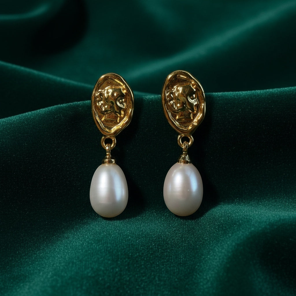 Charmluna gold textured oval stud earrings with white pearl drops on a dark green satin background.