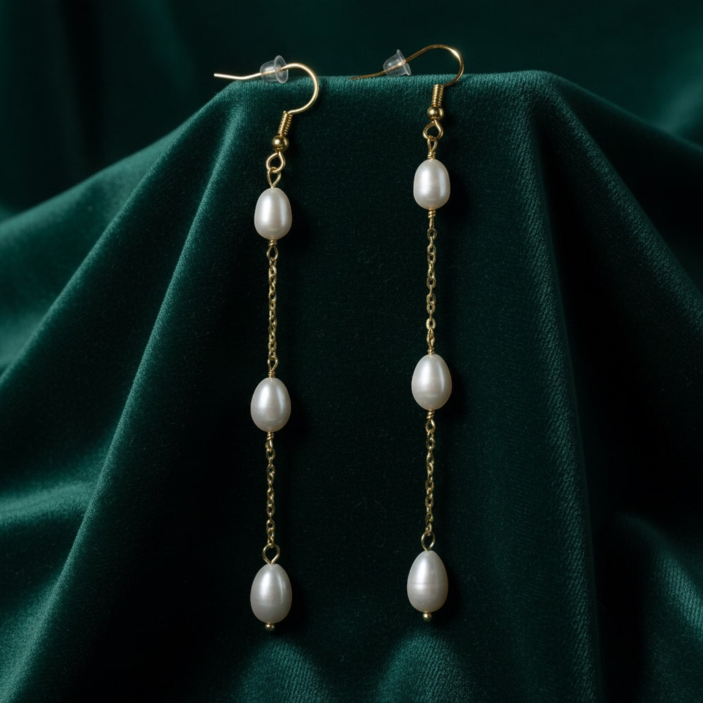 Charmluna long gold-tone chain drop earrings featuring delicate oval pearl accents on a dark green velvet background.