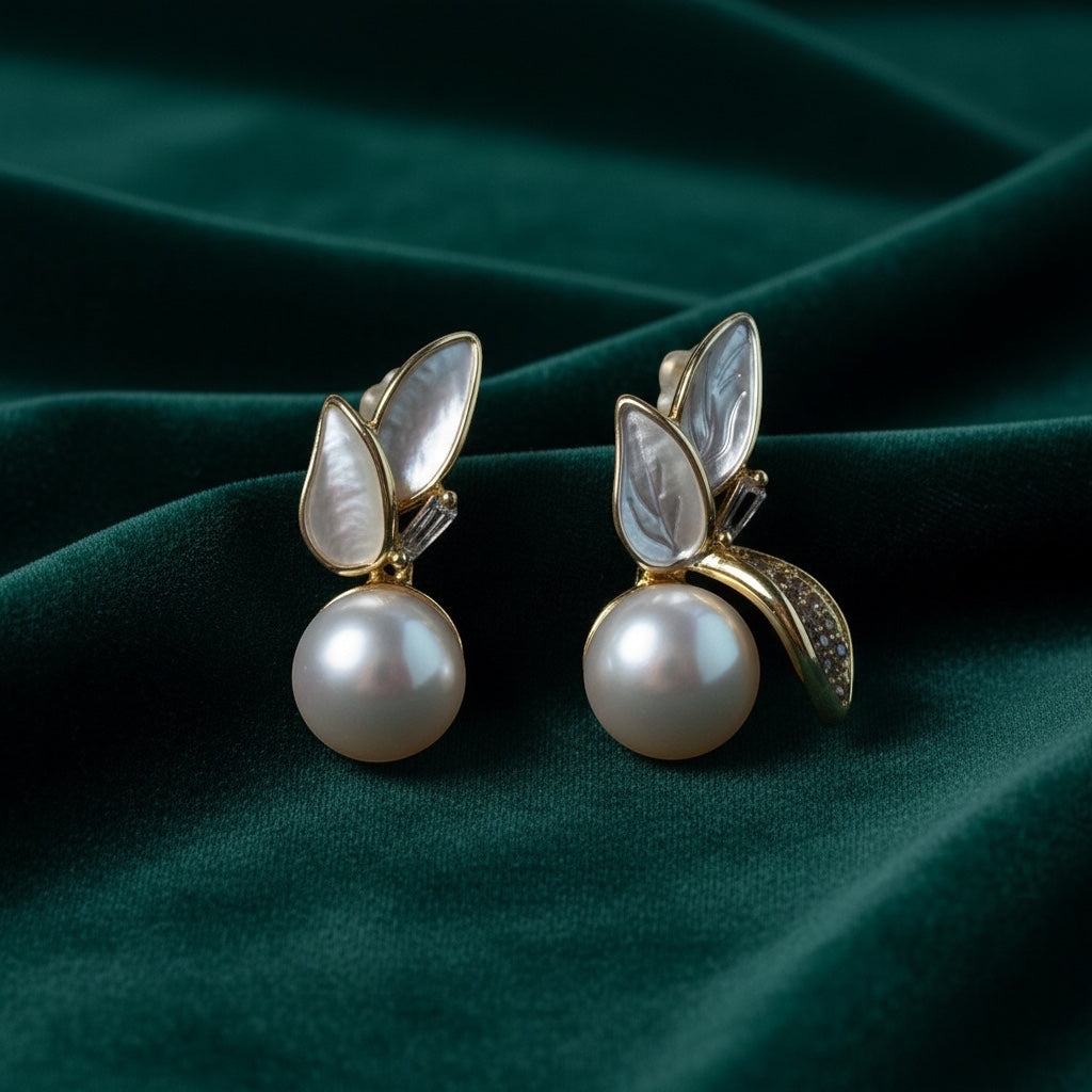 Charmluna leaf stud earrings featuring mother of pearl, round pearls, and gold-tone crystal accents on green velvet.